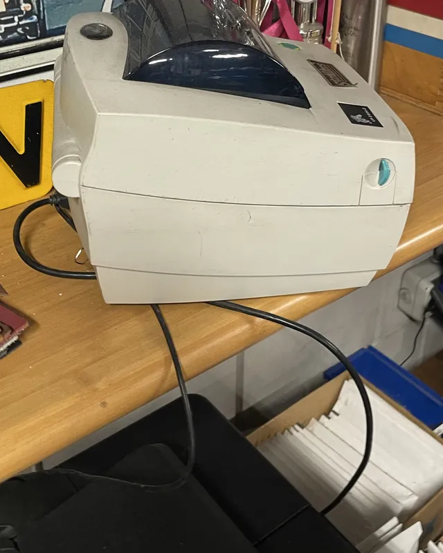 An older Zebra LP 2844-Z label printer on a wooden shelf in the garage, with its USB cable running down